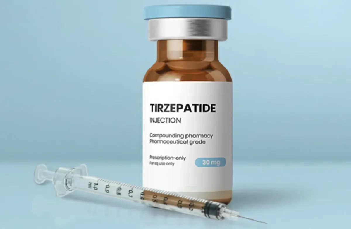 Tirzepatide injection vial and syringe on a light blue surface.